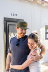 a man and woman hugging in front of a Zilker Belts Greenbelt Rope Hat